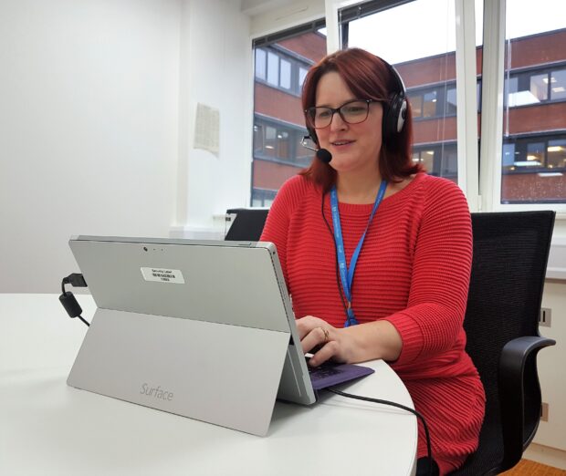 A lady (Tanya) working at a laptop with a headset on. 