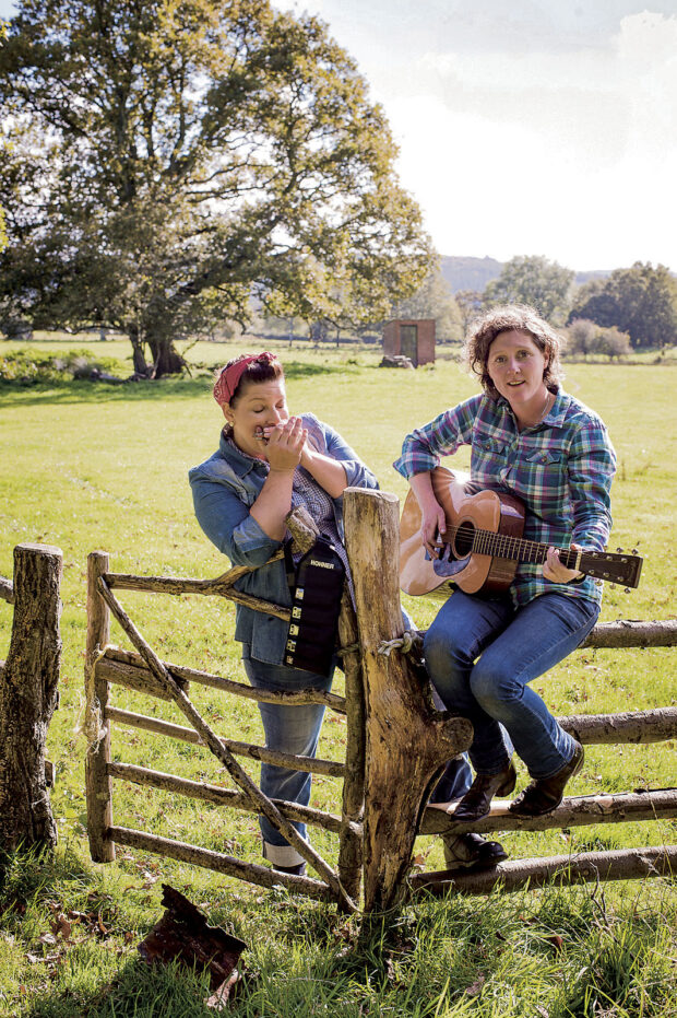 Sam and Shauna in a sunny field resting by a gate and Shauna is playing guitar