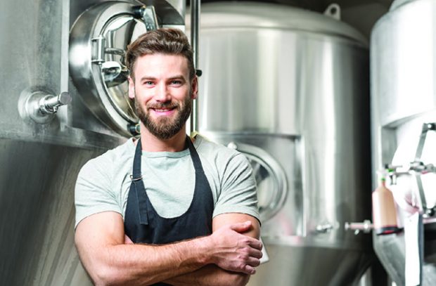 A man standing in front of large metal brewing containers. 