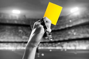 Referee's hand holding whistle and yellow card.