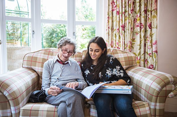 A woman sat on a sofa with an elderly lady reading a book.