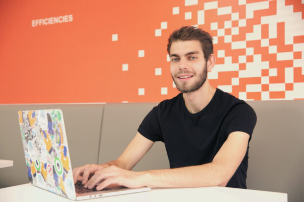 John Richards, systems analyst at Companies House sat down working on a laptop and smiling at the camera.