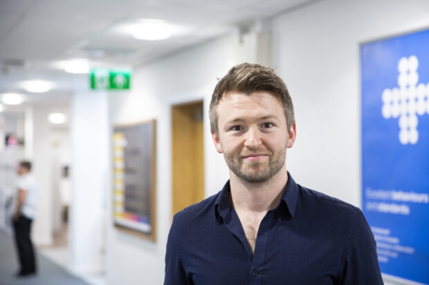 Tom Skidmore, recruitment manager at Companies House standing in Companies House office and smiling at the camera. 