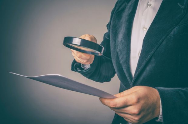 A man in a suit jacket holding a magnifying glass to a piece of paper.