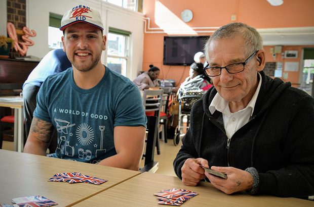 A young volunteer playing cards with an older man at an AGE UK event