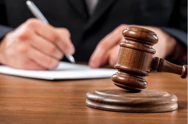 A close up of a judge's gavel and a hand signing a document.