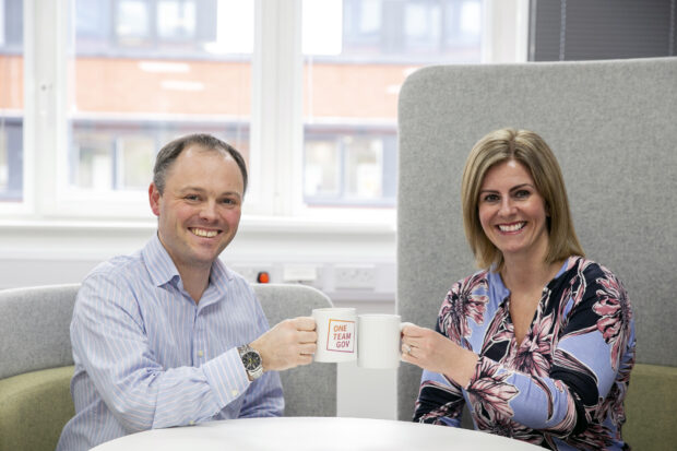 A man and woman holding mugs of coffee and smiling at the camera. 