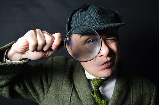 An actor dressed as Sherlock Holmes holding a magnifying glass