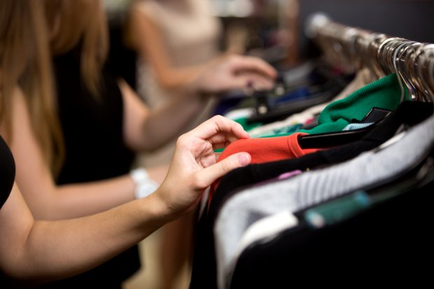 A close up of women browsing clothes on hangers.