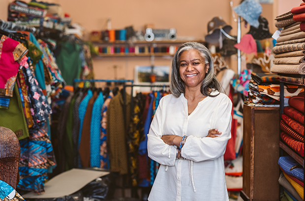 Smiling fabric shop owner standing with her arms crossed by racks and shelves full of colorful textiles