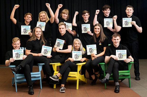 A group of young entrepreneurs in black t-shirts smile at the camera while holding up their ‘Bonnie the Beltie’ children’s book.