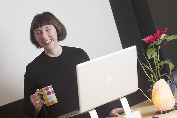 A lady holding a cup of coffee in front of a laptop and smiling. 