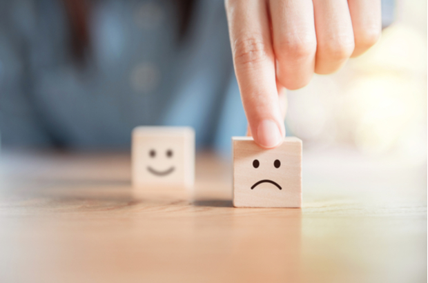 Two cubes with faces drawn on them, one happy and one sad. Person pushing the sad one closer to the camera.