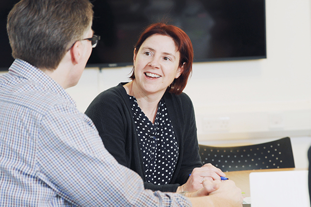 Two colleagues having a onversation at a desk.