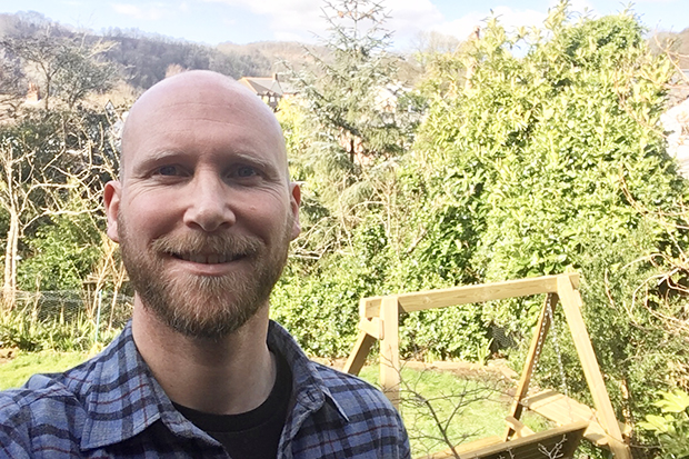 A man smiling at the camera outside in a garden.