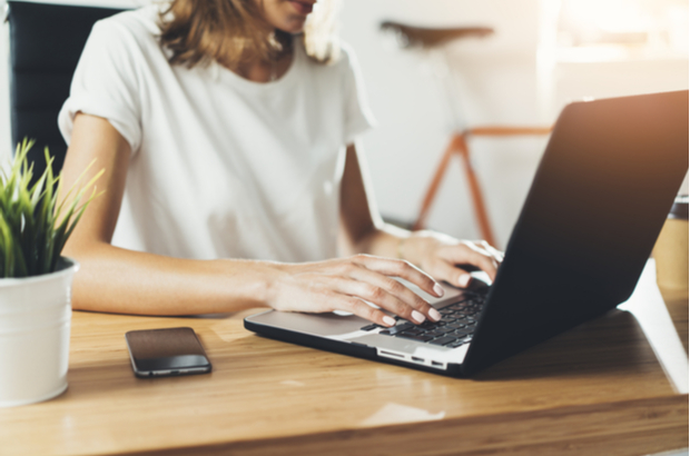 A lady's hands working on a laptop on a desk.