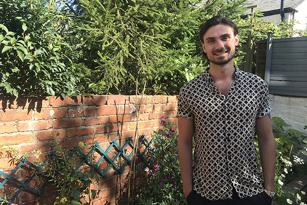 A smiling man standing in a garden with lots of trees and shrubbery.