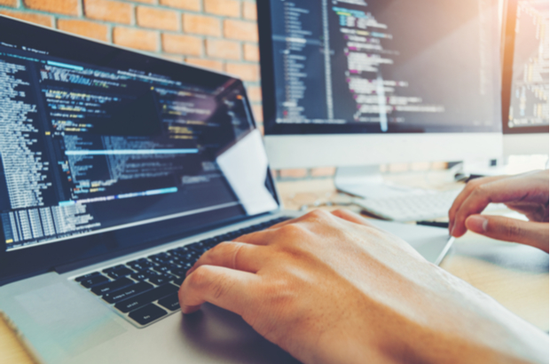 Hands working on a laptop that's displaying a coding programme.