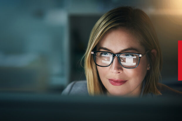 A person working at a computer, with the screen reflecting in their glasses. 