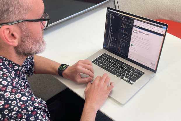 A man working at a desk on a laptop with a Companies House service on the screen.