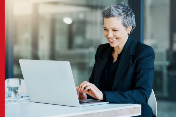 A formally dressed woman smiles as she types on a laptop