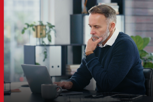 A smartly dressed man sits in an office, looking at a laptop screen