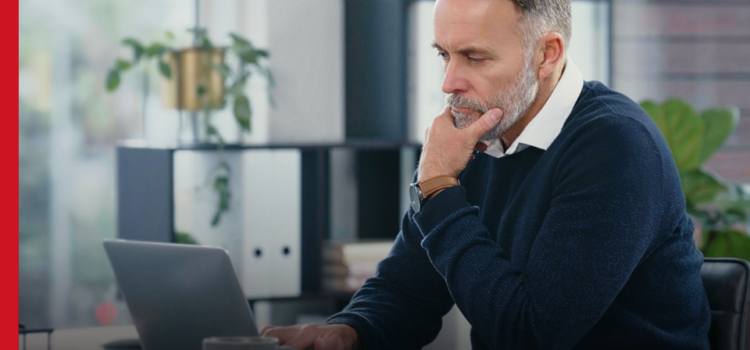 A smartly dressed man sits in an office, looking at a laptop screen
