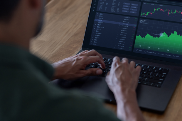 A man types on the keyboard of a laptop. The screen shows graphs and data