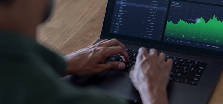 A man types on the keyboard of a laptop. The screen shows graphs and data.